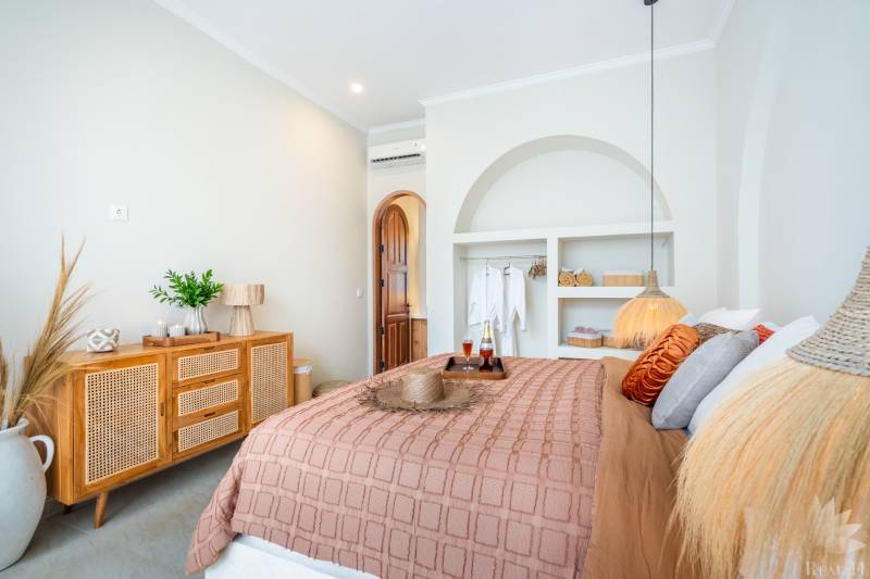 Világos hálószoba a villában természetes dekorációkkal, lágy világítással és kényelmes ággyal.