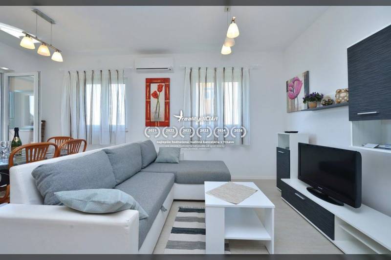 Nappali egy kétszobás lakásban kényelmes kanapéval, fehér bútorokkal és televízióval.