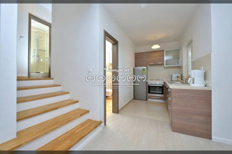 Konyha és fa dekorációjú lépcső vezet a fürdőszobához egy kétszobás lakásban.