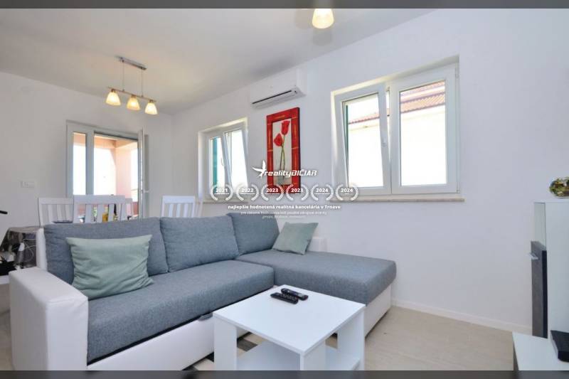 Nappali szürke kanapéval, dohányzóasztallal és étkezőasztallal egy kétszobás lakásban.