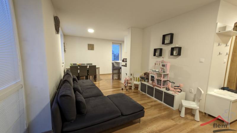 Nappali egy kétszobás lakásban fa mintázatú padlóval és gyereksarokkal.