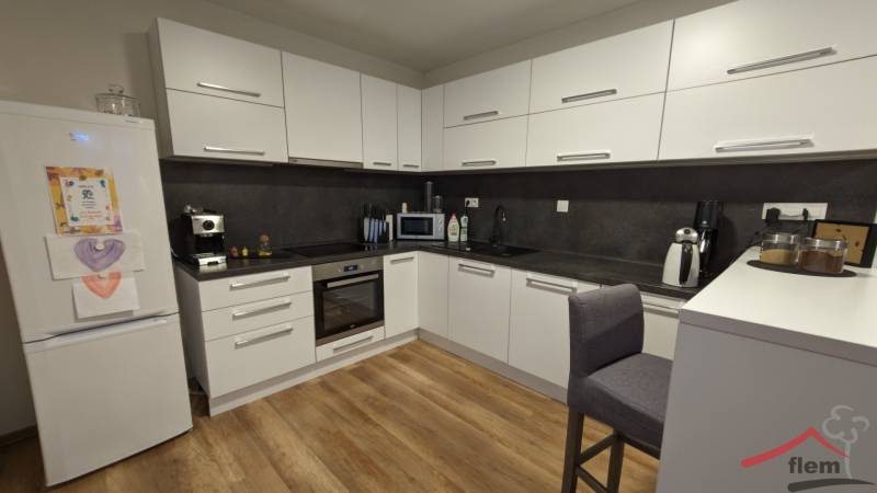 Két szobás lakás konyhája fa dekor padlóval és fehér szekrényekkel.