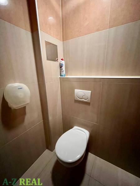 Iroda csempézett mosdója tisztítószerrel és WC-papír adagolóval.