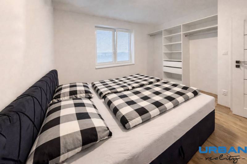 Hálószoba egy háromszobás lakásban, beépített szekrénnyel és fa dekor padlóval.