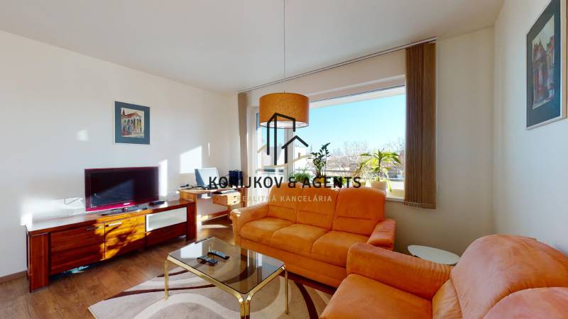 Nappali egy kétszobás lakásban narancssárga kanapéval és TV-vel, fa mintázatú padlóval.