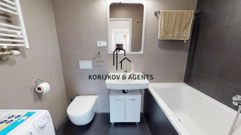 Fürdőszoba káddal, mosdóval, függesztett WC-vel és mosógéppel egy kétszobás lakásban.