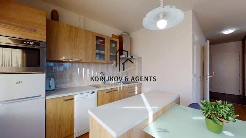 Két szobás lakás konyhája fa dekorral, felszerelve háztartási gépekkel és világítással.