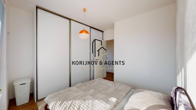 Hálószoba egy kétszobás lakásban tolóajtós szekrénnyel és padlón lévő ággyal fa dekorációval.