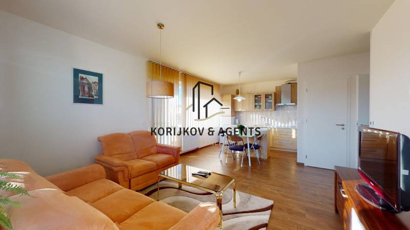 Nappali narancssárga kanapéval, asztallal és fa dekorációjú padlóval egy kétszobás lakásban.