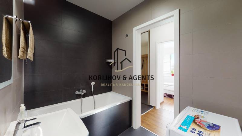 Fürdőszoba egy kétszobás lakásban káddal és mosógéppel, fa dekoros padlóval.