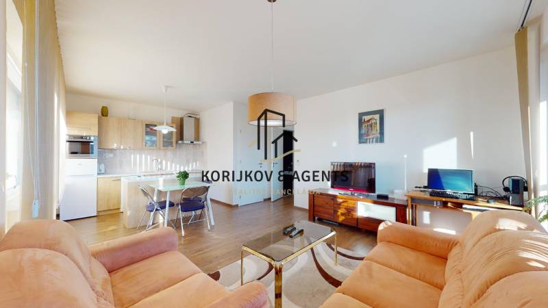 Nappali konyhasarokkal, kanapékkal és fa dekorációjú padlóval egy kétszobás lakásban.