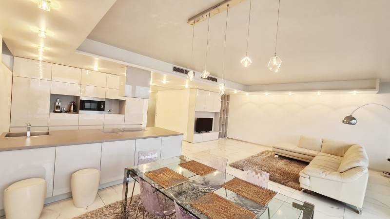 Tágas nappali egy háromszobás lakásban konyhával, étkezőasztallal és kényelmes kanapéval.