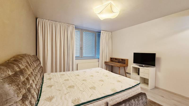 Hálószoba egy háromszobás lakásban ággyal, televízióval és íróasztallal.