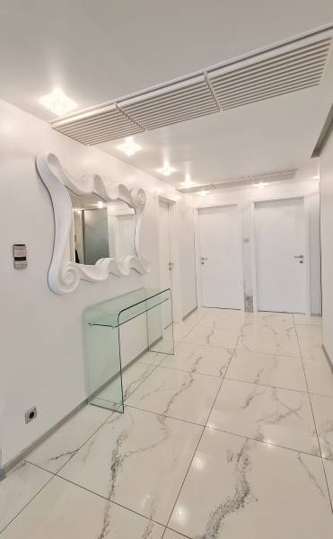 Háromszobás lakás belső tere fényes csempékkel, tükörrel és üvegasztallal.