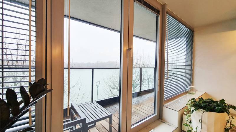 Erkély kilátással a folyóra, üvegajtók, fa dekorációjú padló.