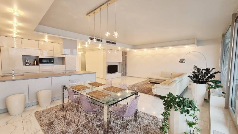 Tágas belső tér egy 3 szobás lakásban konyhával, étkezőasztallal és nappali résszel.