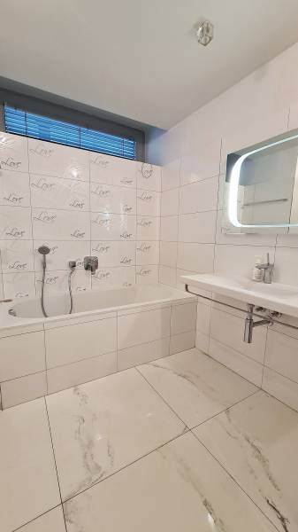 Fürdőszoba káddal és csempékkel egy háromszobás lakásban, fehér és szürke színárnyalatokban.