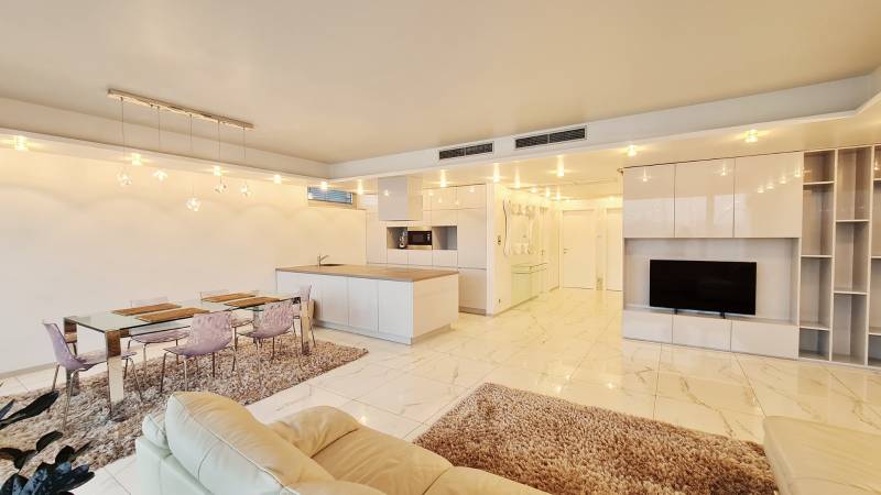 Nappali konyhaszigettel, étkezőasztallal és TV-vel egy háromszobás lakásban.