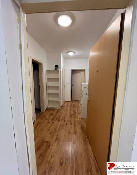 Folyosó egy kétszobás lakásban, fa mintázatú padlóval és polcokkal a falon.