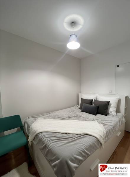 Hálószoba egy kétszobás lakásban fehér bútorokkal, szürke kiegészítőkkel és egy székkel.