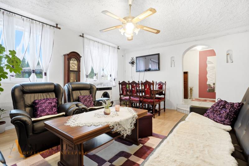 Nappali családi házban kandallóval, fekete kanapékkal és fa dekoros padlóval.