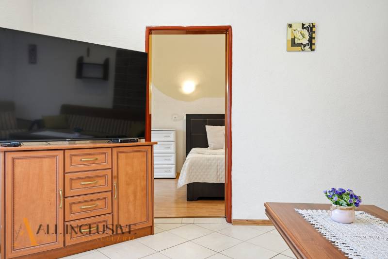 Családi ház belső tere nagy televízióval, nyitott ajtó a hálószobába, dekorációk.