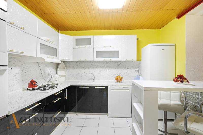 Konyha családi házban világos szekrényekkel, márványburkolattal és fehér háztartási gépekkel.