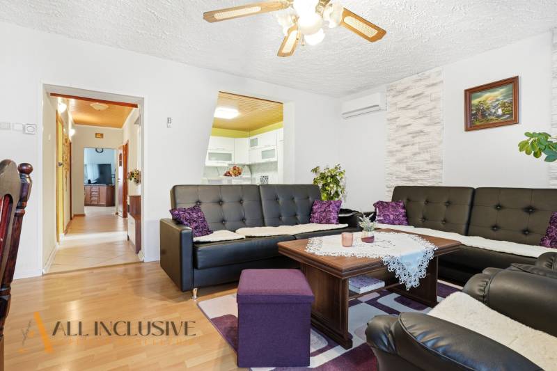 Nappali egy családi házban, fa mintázatú padlóval és fekete bőr kanapékkal.