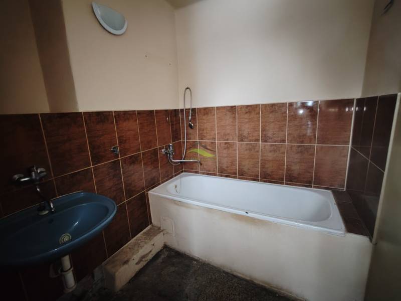 Fürdőszoba barna csempékkel, káddal és kék mosdóval egy kétszobás lakásban.