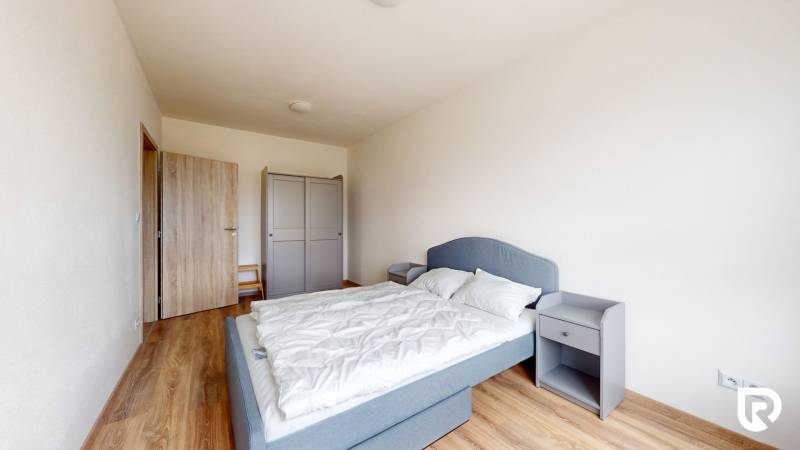 Hálószoba egy háromszobás lakásban, fa dekoros padlóval, szürke ággyal és gardróbbal.