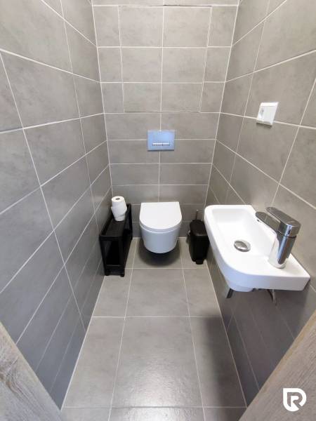 Fürdőszoba fali WC-vel, mosdóval és szürke csempékkel egy háromszobás lakásban.