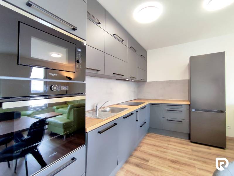 Konyha egy háromszobás lakásban, fa dekor padlóval, szürke szekrények, beépített készülékek.