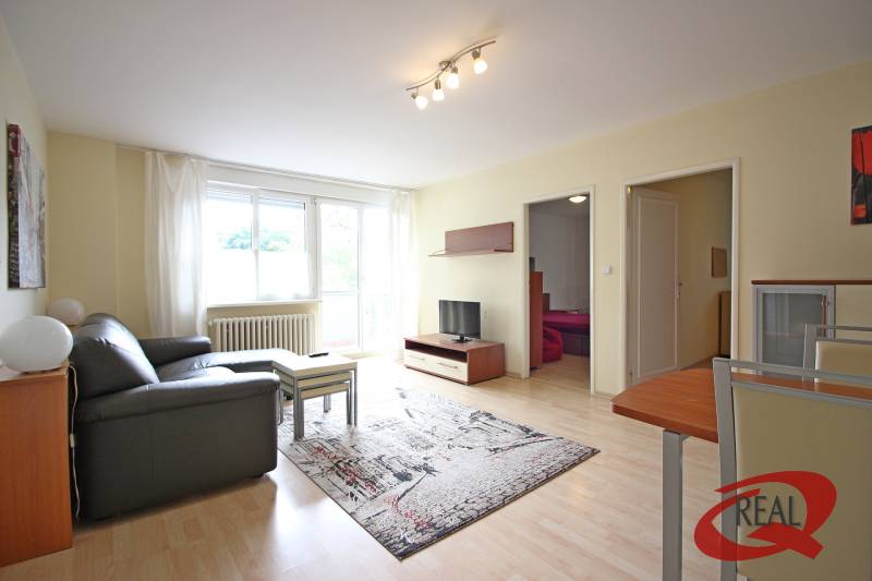 A háromszobás lakás nappalija kanapéval, asztallal és televízióval, fa dekorációjú padlón.