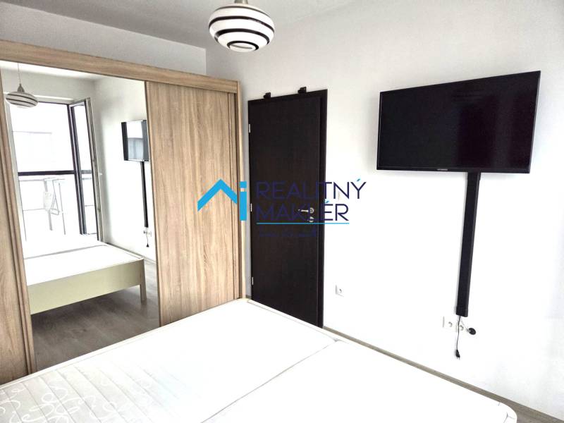 Hálószoba televízióval, ruhásszekrénnyel és faajtóval egy garzonlakásban.