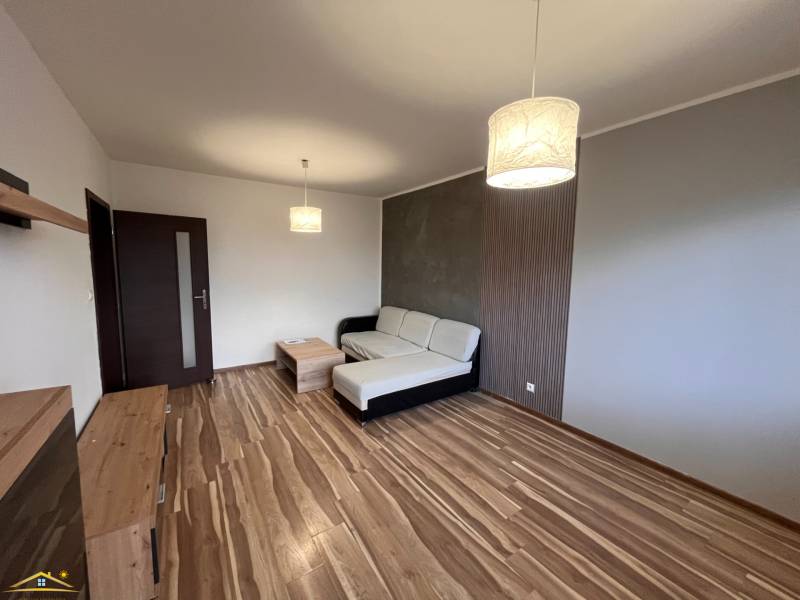 Nappali egy kétszobás lakásban fa dekor padlóval, kanapéval és lámpával.