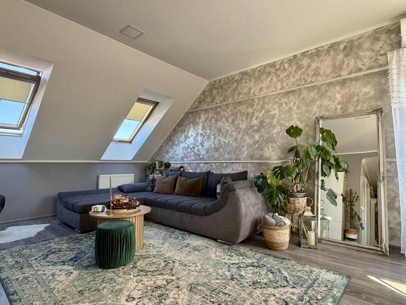 Nappali egy kétszobás lakásban, fa hatású padlóval, kihúzható kanapéval és növényekkel.