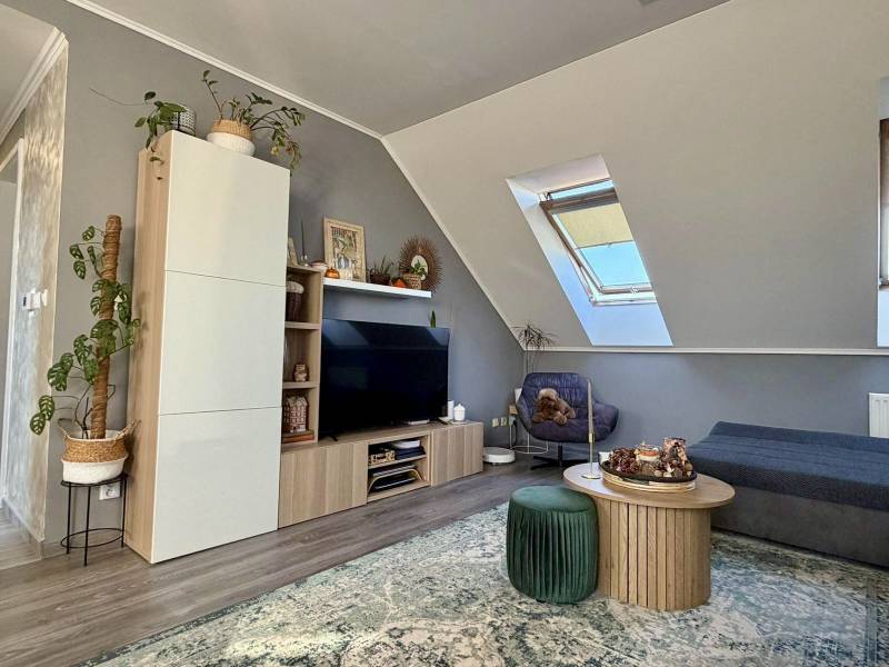 Nappali egy kétszobás lakásban tetőablakkal, fa dekor padlóval, kényelmes bútorokkal.