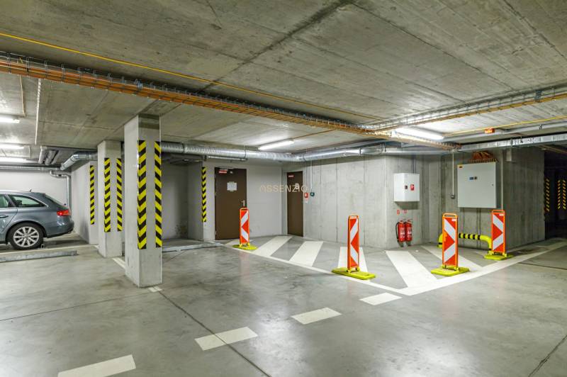 Földalatti garázs parkolóhellyel, figyelmeztető táblákkal és tűzoltó készülékekkel.