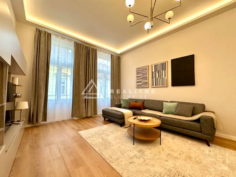 Nappali egy kétszobás lakásban, fa mintázatú padlóval, szürke kanapéval és dekoratív képekkel.