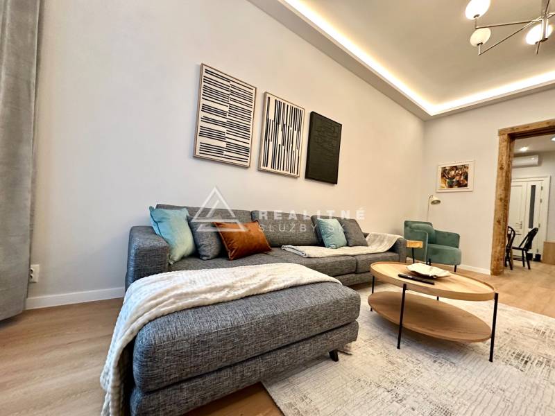 Nappali kanapéval, fa hatású padlóval és műalkotásokkal egy kétszobás lakásban.