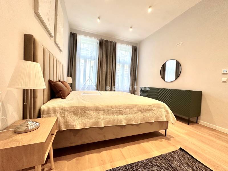 Hálószoba egy kétszobás lakásban nagy ággyal, lámpával és fa dekorációjú padlóval.