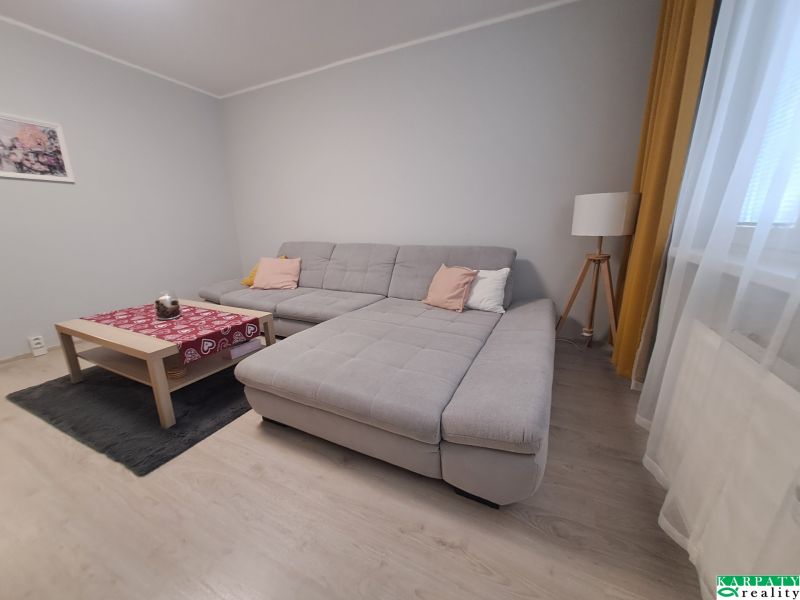 Nappali egy háromszobás lakásban kanapéval és fa dekorációjú padlóval.