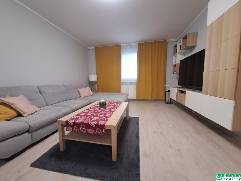 Nappali egy háromszobás lakásban kanapéval, dohányzóasztallal és fa dekorációjú padlóval.