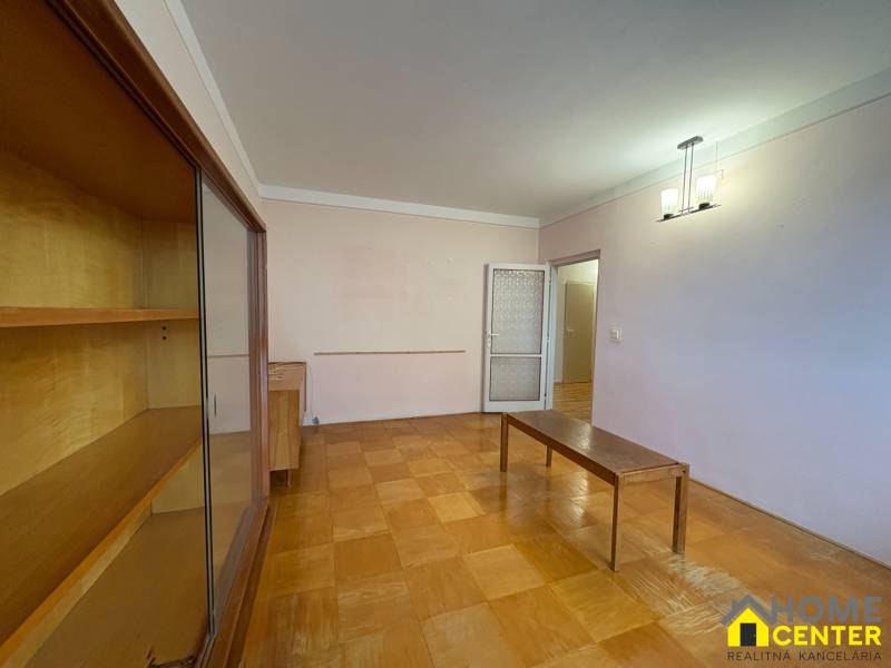 Nappali egy háromszobás lakásban, fa hatású padlóval és bútorokkal.