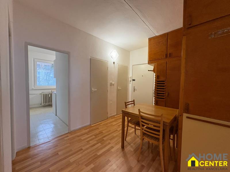 3 szobás lakás belső tere fa mintázatú padlóval, étkező sarok asztallal és székekkel.