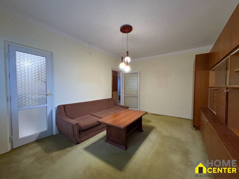 Nappali egy háromszobás lakásban kanapéval, dohányzóasztallal és vitrinnel.