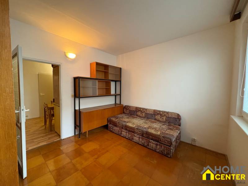 Szoba egy háromszobás lakásban kanapéval, szekrénnyel és fa mintázatú padlóval.