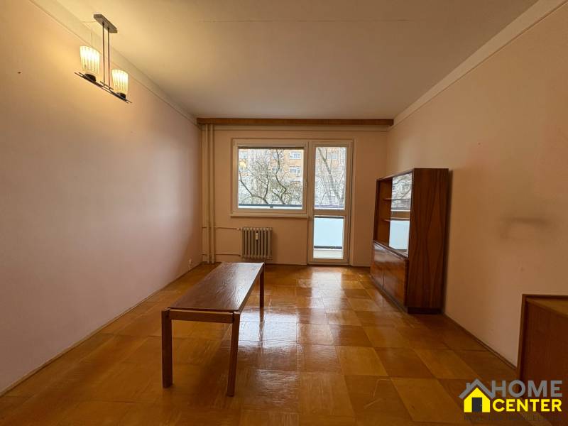 Nappali egy háromszobás lakásban, fa dekoros padlóval és egyszerű bútorokkal.