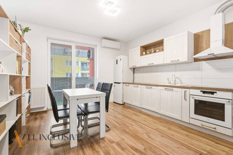 Konyha egy kétszobás lakásban fehér szekrényekkel és fa mintázatú padlóval.