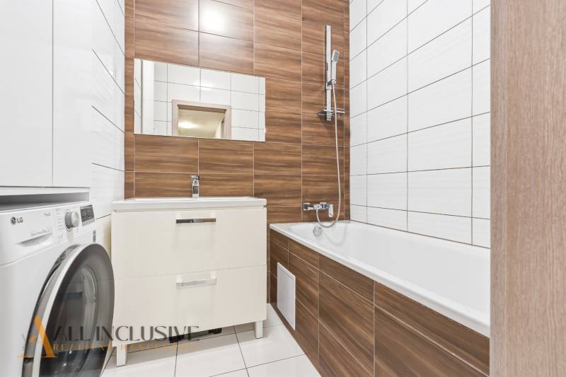 Kétszobás lakás fürdőszobája káddal, mosdóval és mosógéppel. Fa dekoráció használata.